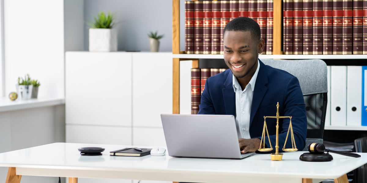 Law clerk at modern legal office desk reviewing documents on laptop with law library books and scales of justice, representing entry-level legal careers in Canada