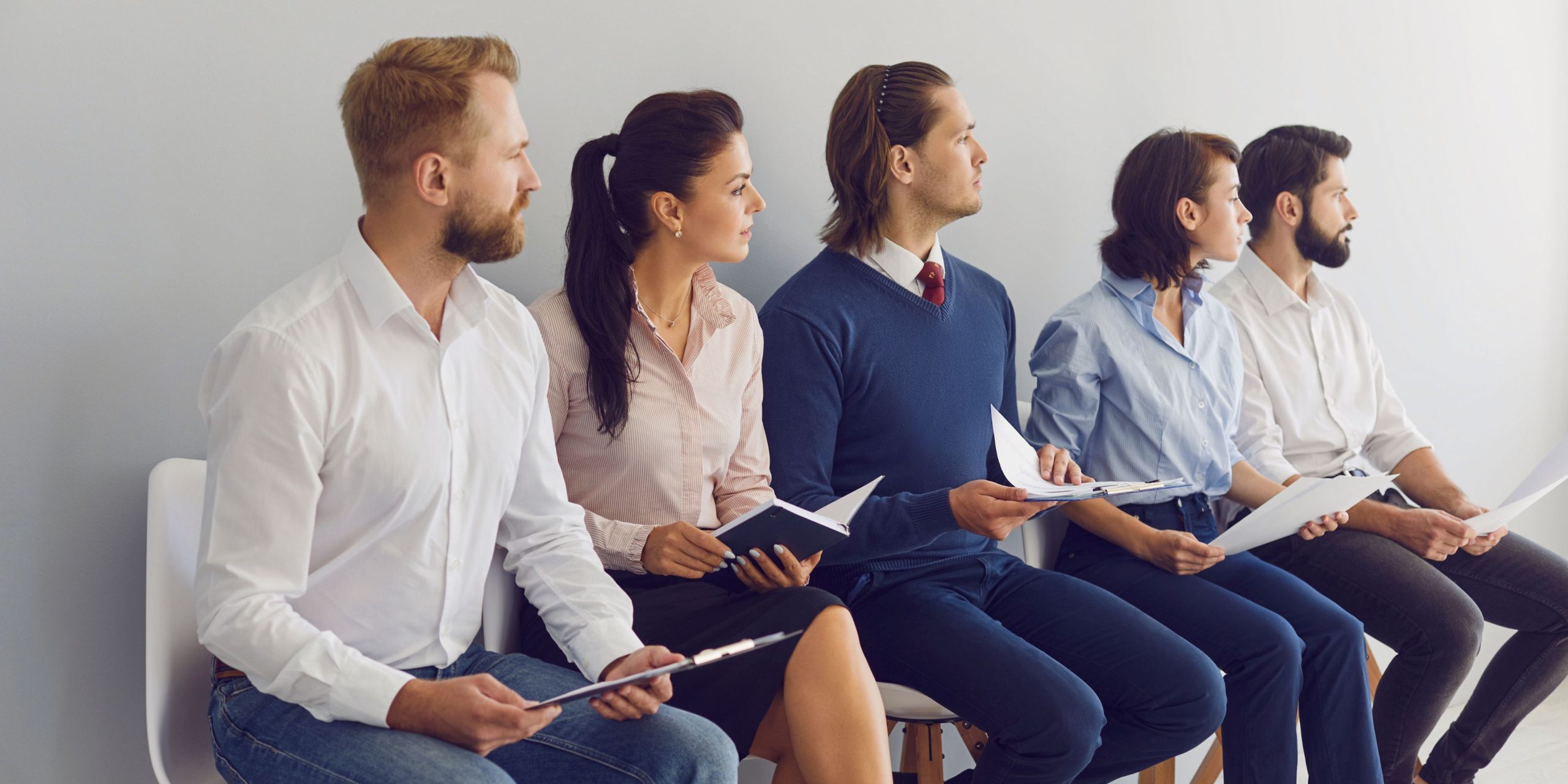 A group of professionally dressed candidates seated in a waiting area, holding resumes and preparing mentally for their job interviews.