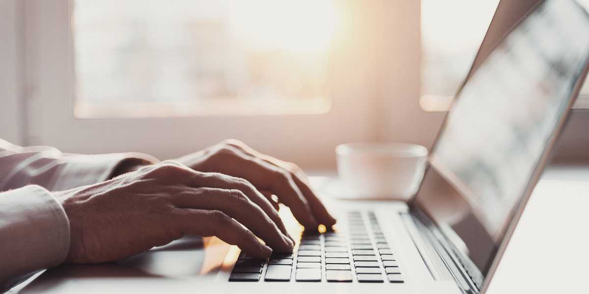 Microsoft Office software package Side view of hands typing on laptop keyboard in warm-lit workspace with coffee cup nearby, representing the flexibility of Microsoft Office 365 for remote work capabilities.
