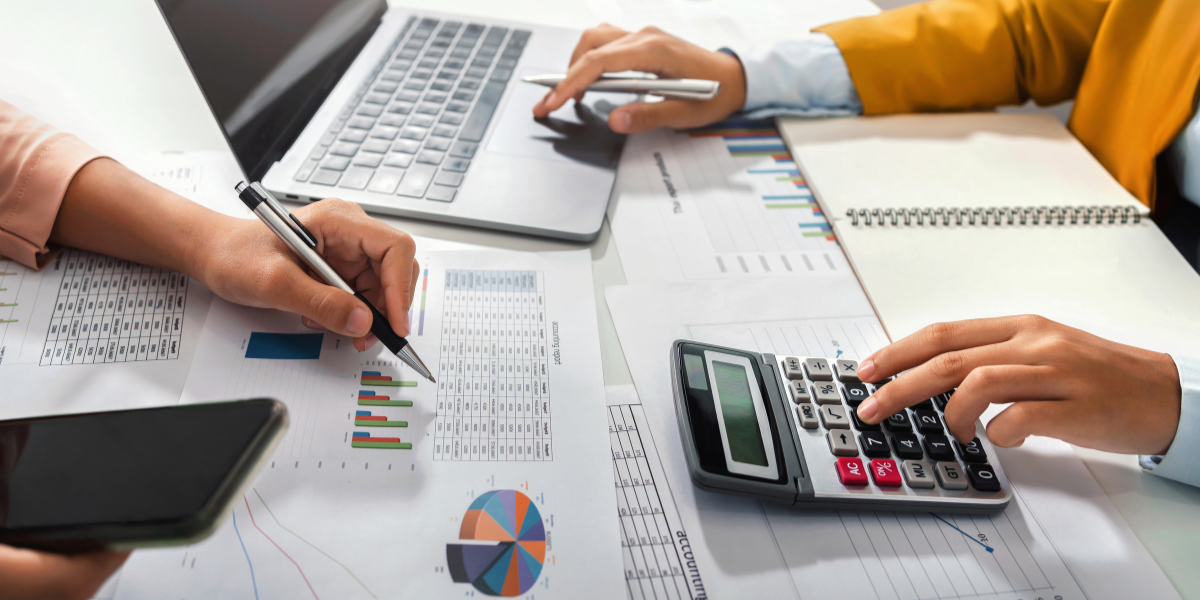 Bookkeeper in professional attire working with calculator, financial statements and laptop - illustrating the professional nature of Canadian accounting roles available without university qualifications.