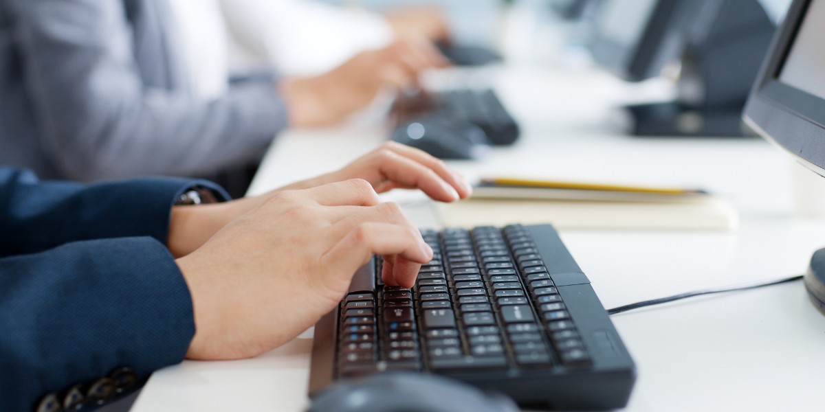 Business professionals practicing touch typing techniques at keyboards in a Canadian office, demonstrating proper hand placement for WPM typing certification preparation.